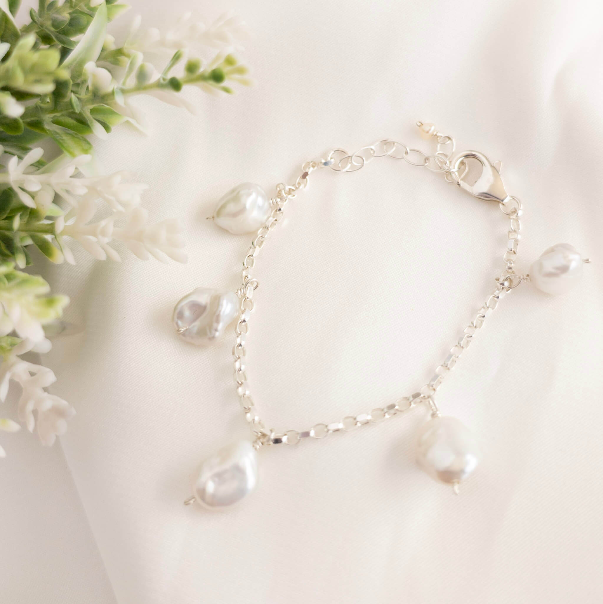 Pearl bracelet on a white surface with flowers in the background