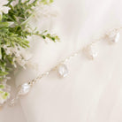 Pearl bracelet with teardrop pendants on a light background with greenery