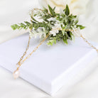Gold chain necklace with a pearl pendant on a white surface with greenery