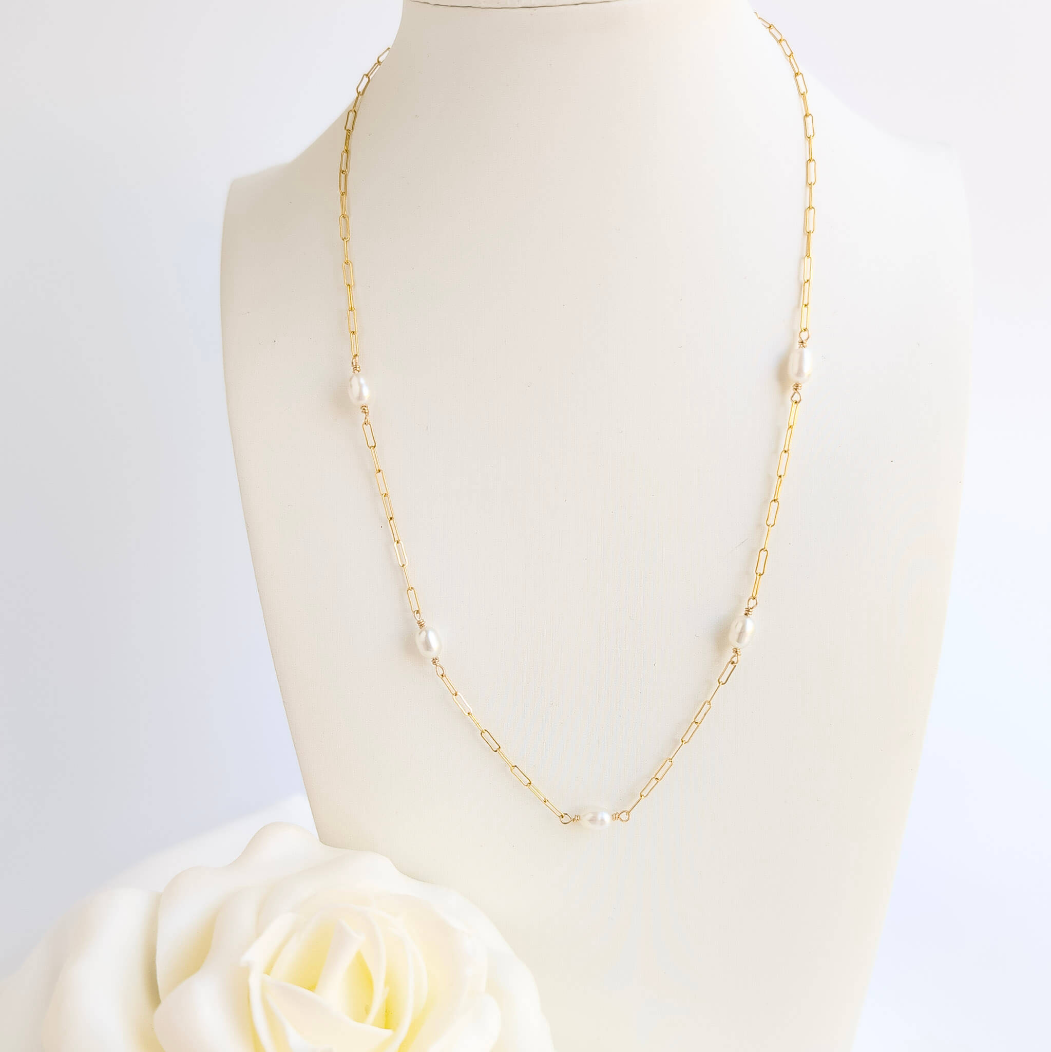 Gold chain necklace on a mannequin with a white rose in the foreground