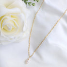 Gold chain necklace with a pearl pendant on a white surface with a white rose.