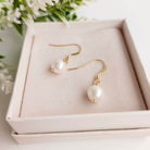 Pearl earrings on a pink jewelry box with flowers in the background
