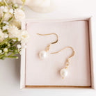 Pearl earrings with gold hooks on a pink box with flowers in the background