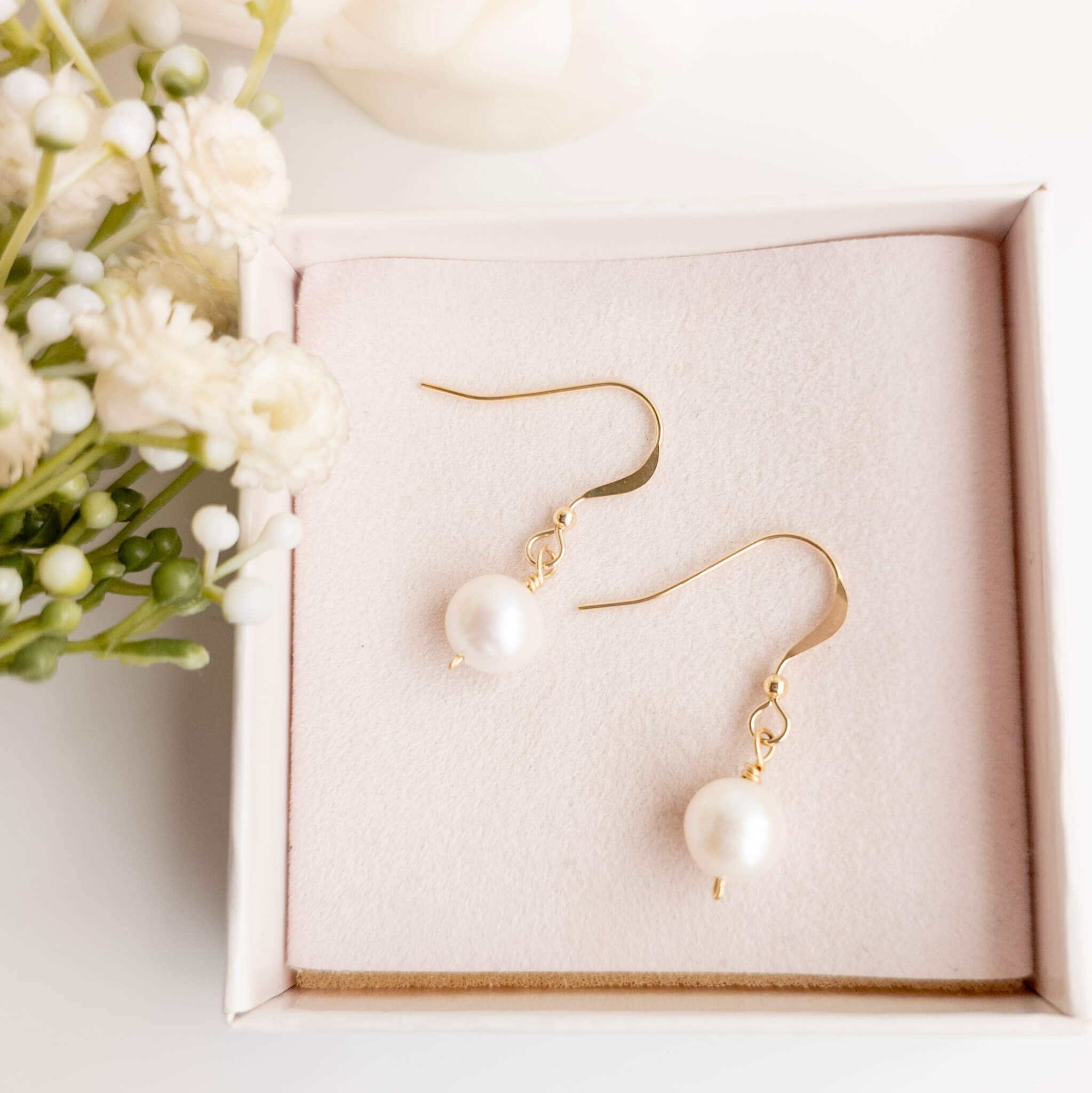 Pearl earrings with gold hooks on a pink box with flowers in the background