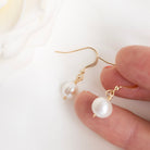 Pearl earrings with gold hooks held by a hand on a white background