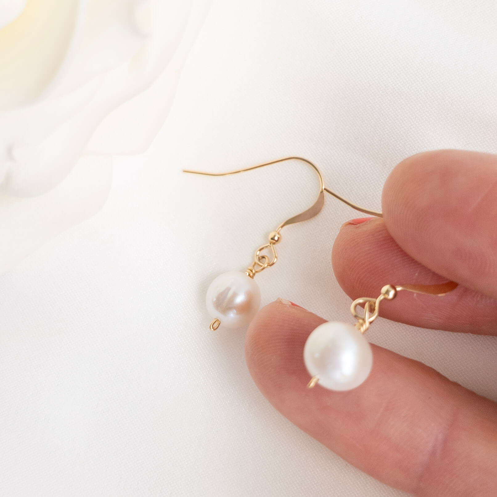Pearl earrings with gold hooks held by a hand on a white background