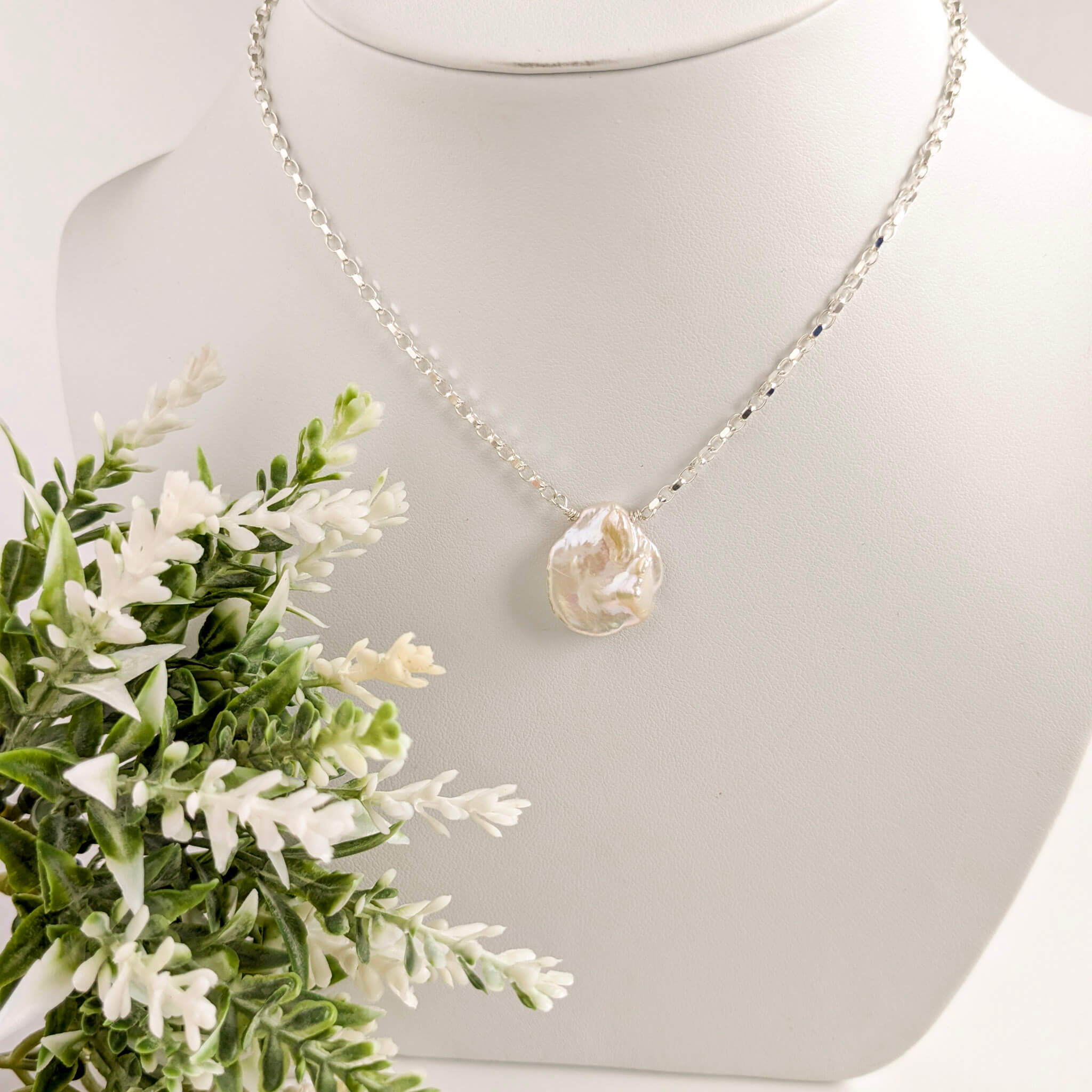 Pearl necklace on a mannequin bust with greenery
